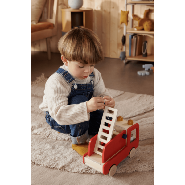 Un petit garçon qui joue avec un camion de pompier en bois rouge avec l'échelle levée
